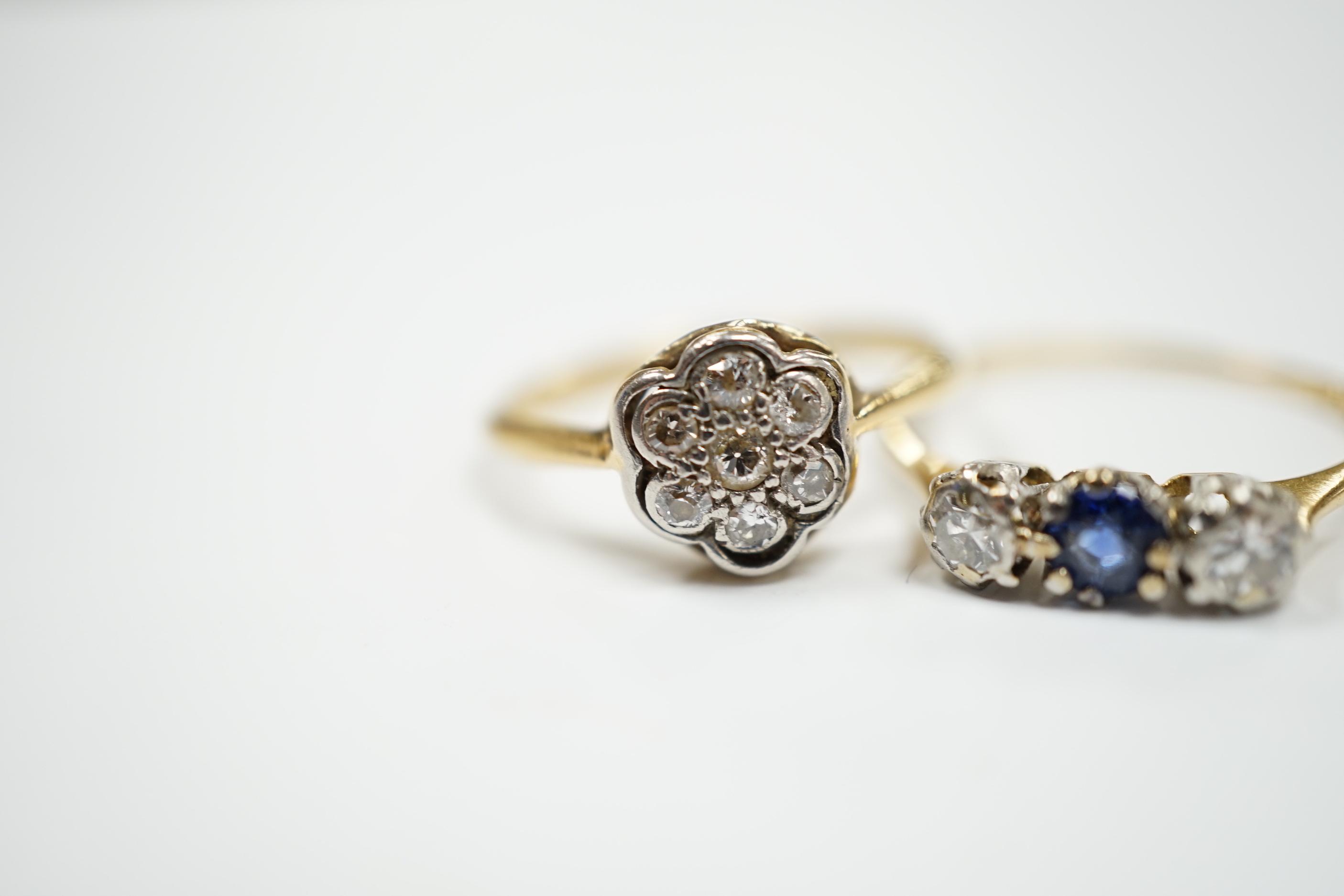 A 1920's 18ct, plat and diamond cluster set flower head ring, size M/N and a 18ct and plat. sapphire and diamond set three stone ring, size O/P, gross 3.9 grams.